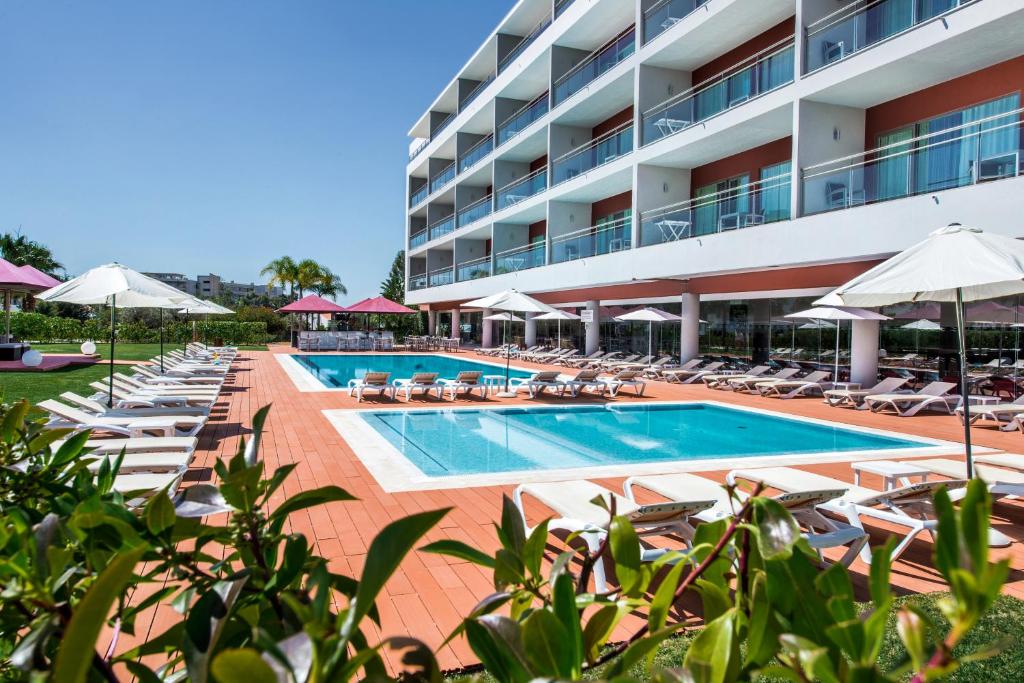 阿尔布费拉Areias Village Beach Suite Hotel的一个带游泳池、椅子和遮阳伞的酒店
