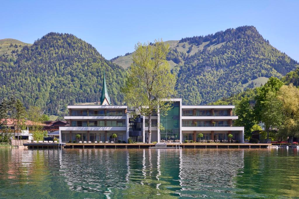 瓦尔赫湖Hotel Das Walchsee的一座水面上的建筑,背景是群山