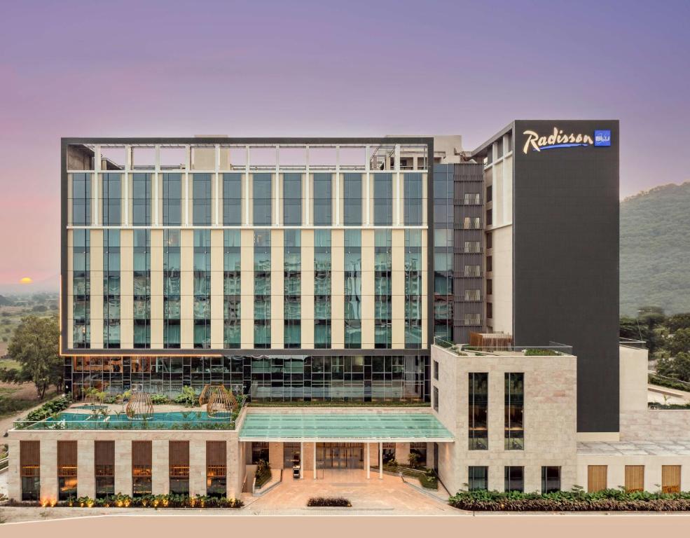 纳西克Radisson Blu Hotel & Spa, Nashik的一座高大的建筑,前面有一个游泳池