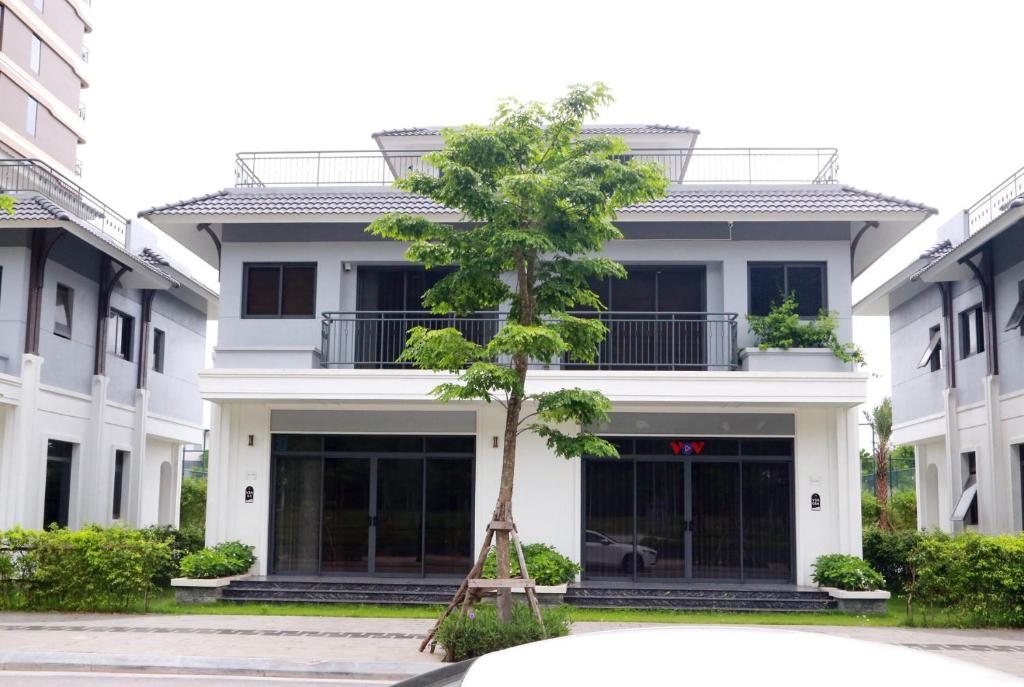 Green Bay Luxury Villa Sonasea Vân Đồn的白色建筑前的树