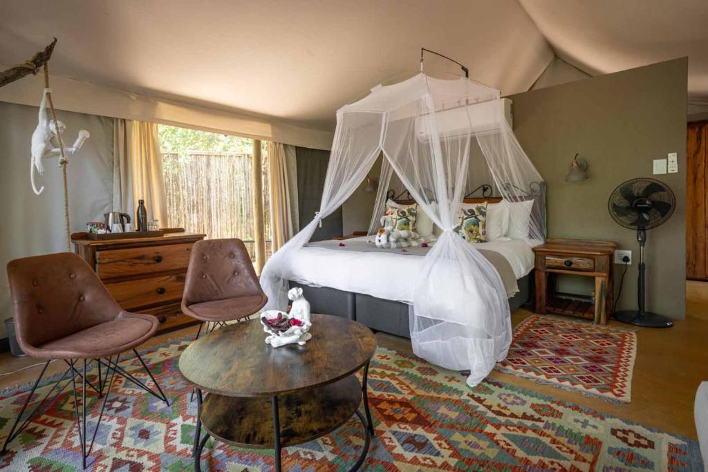 斯库库扎Umkumbe Bush Lodge - Luxury Tented Camp的一间卧室配有一张天蓬床和两把椅子