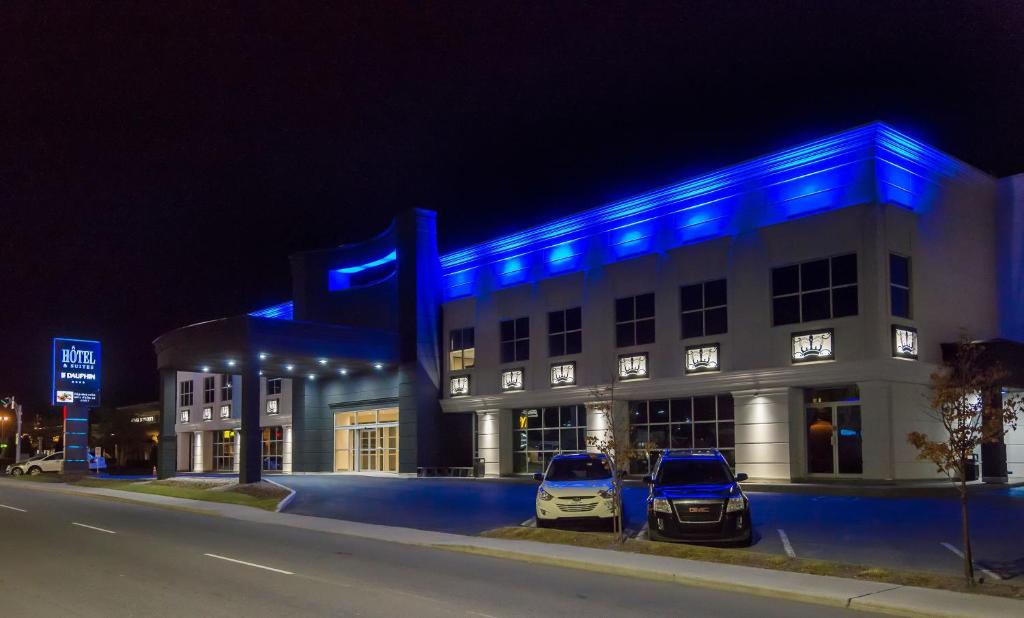 德拉蒙德维尔Hotel & Suites Le Dauphin Drummondville的2辆汽车停在一座蓝色灯光的建筑前