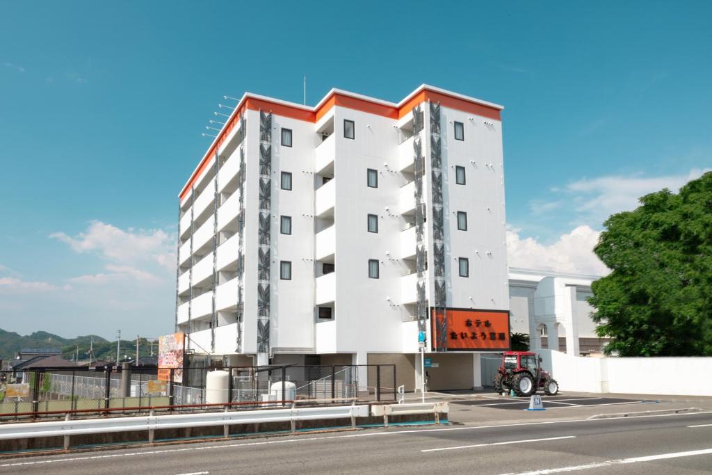 松山Hotel Taiyo Nouen Furumitsu的白色的建筑,在道路的一边有红色的屋顶