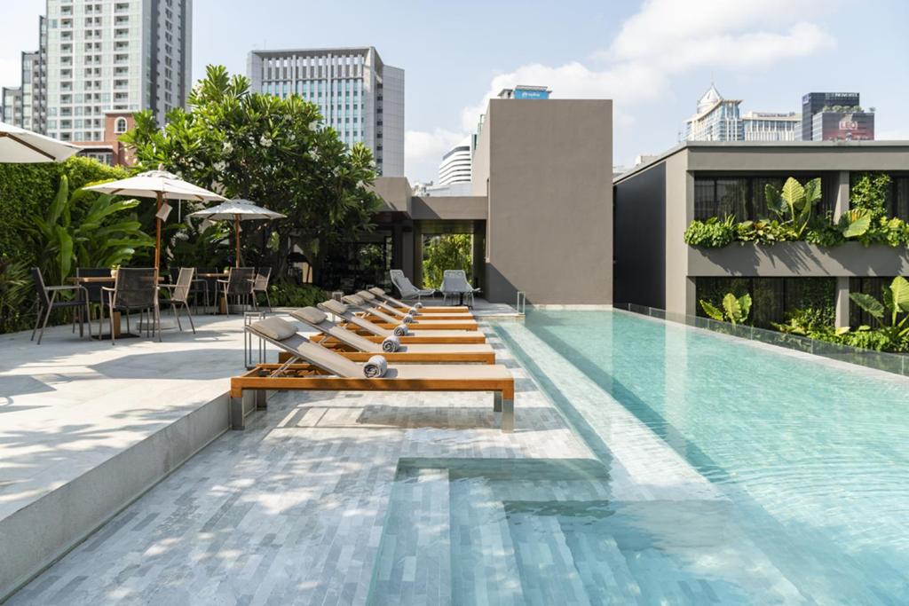 曼谷Ad Lib Hotel Bangkok的一座带长椅的游泳池位于一座建筑的一侧