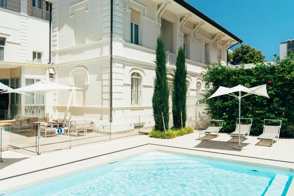 里米尼Hotel Regina Elena 57 & Oro Bianco SPA的一座带椅子和遮阳伞的大楼前的游泳池