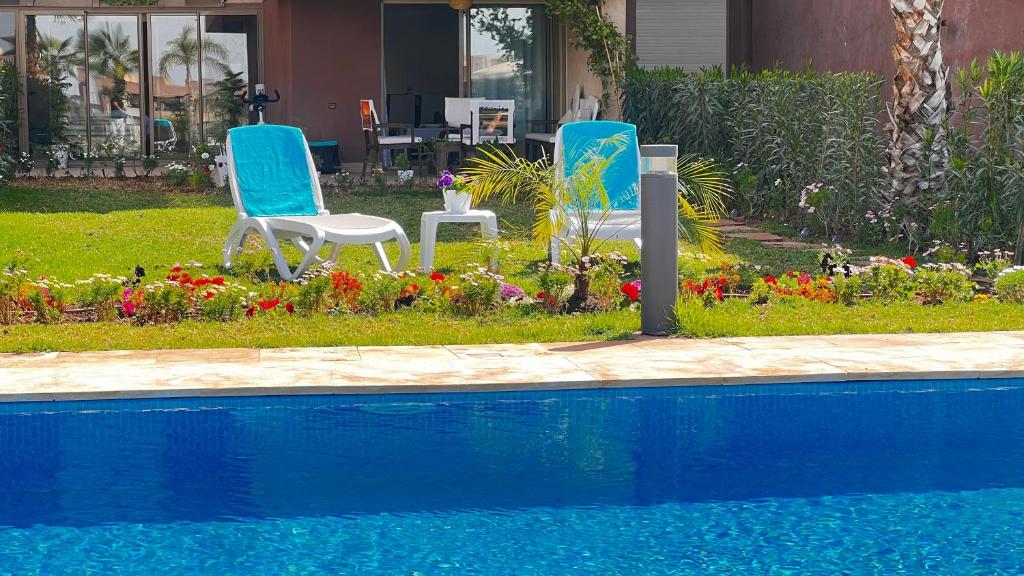 马拉喀什Prestigia,Golf, piscine, soleil, paysage, sport, spacieux,lux résidence的游泳池畔的两把椅子和鲜花