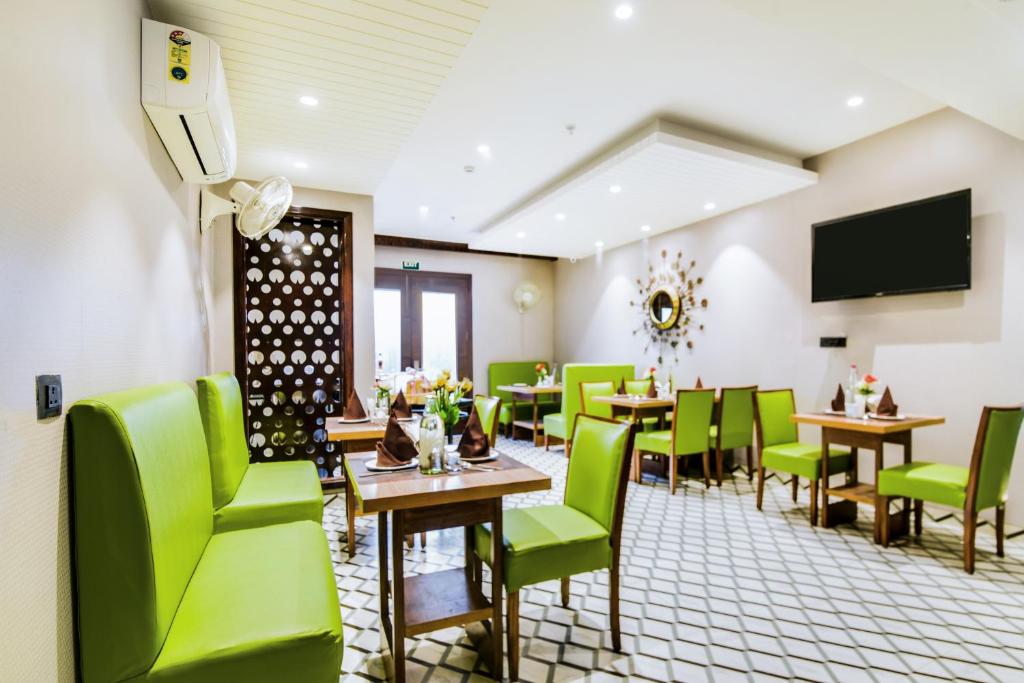 新德里Hotel Bluestone - Nehru Place的餐厅设有绿色的桌椅和平面电视。