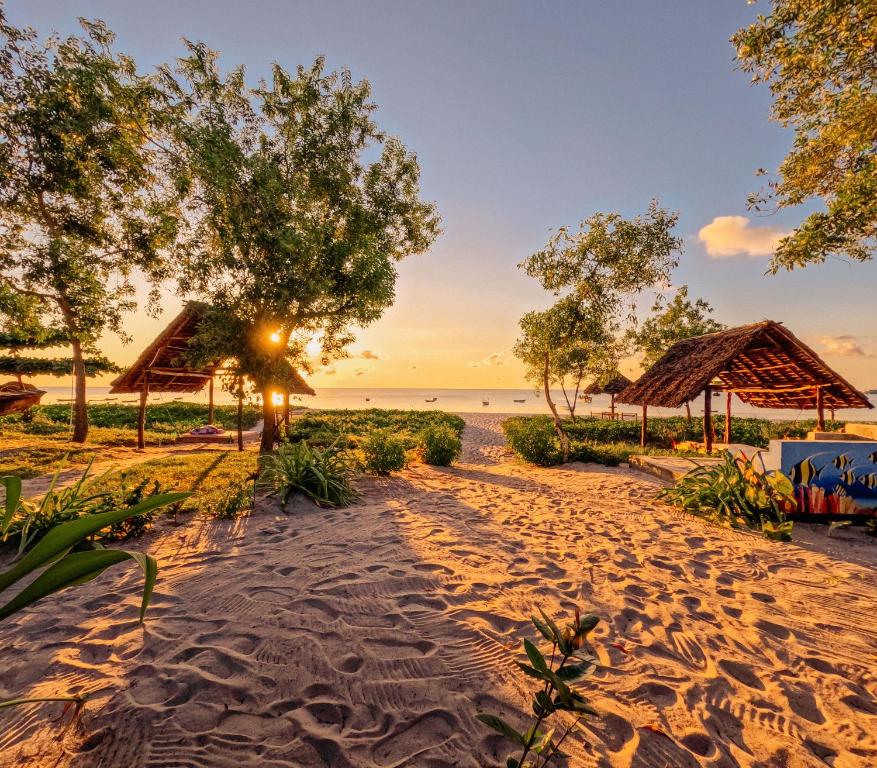 基林多尼Maisara Mafia Beach Lodge的日落时分拥有树木和小屋的海滩