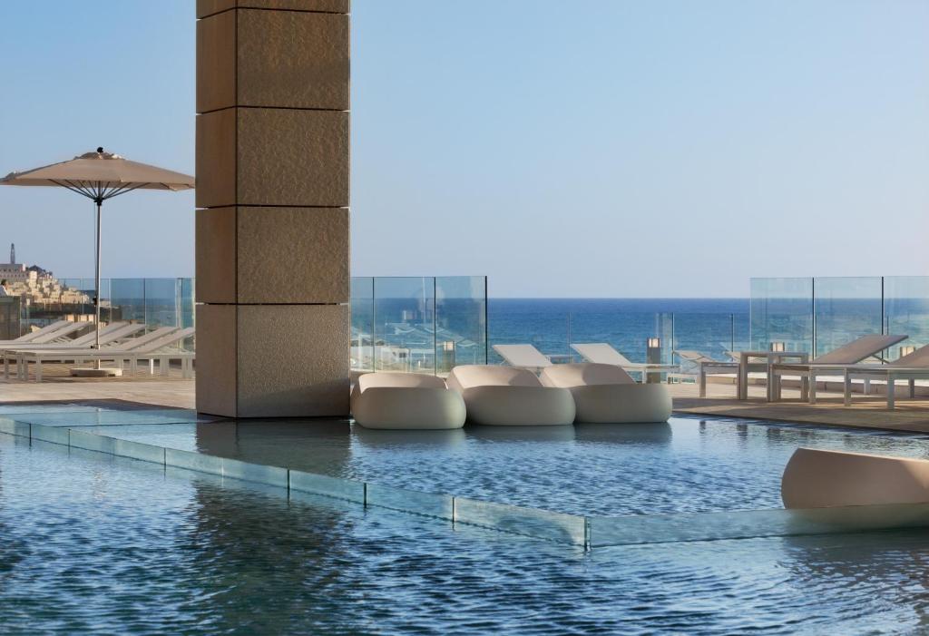 特拉维夫Royal Beach Hotel Tel Aviv by Isrotel Exclusive的一座带白色椅子的游泳池,其背景是大海