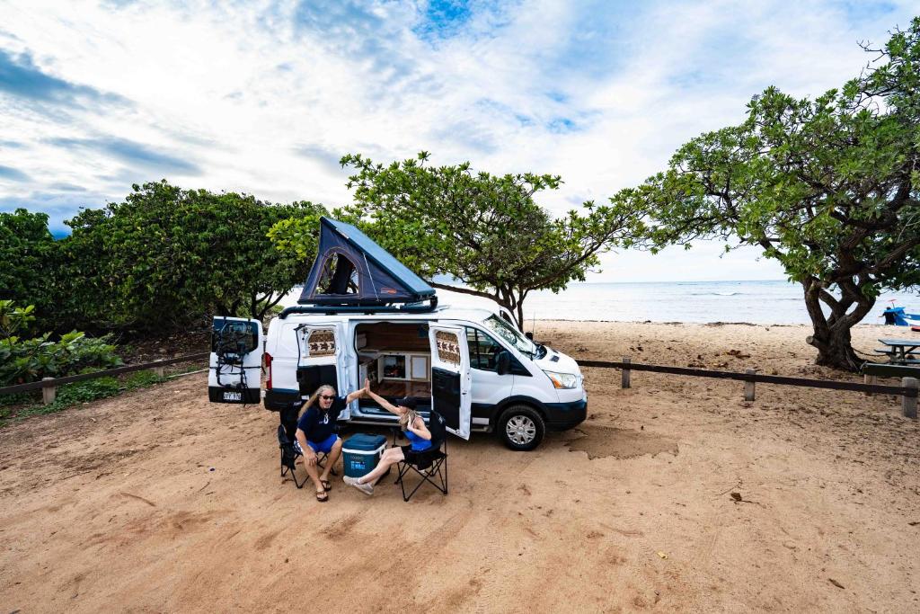 卡胡卢伊CampCar Maui Jeeps SUVs Hybrid Camper van Rentals with equipment and Travel Advice的一群人坐在海滩上一辆面包车前面