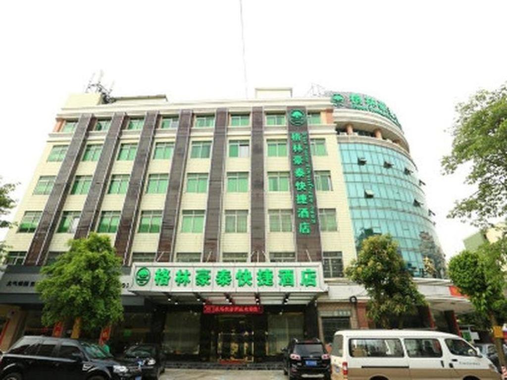 广州GreenTree Inn Guangzhou Baiyun International Airport Huaxi Road Express Hotel的一座大型建筑,前面有汽车停放