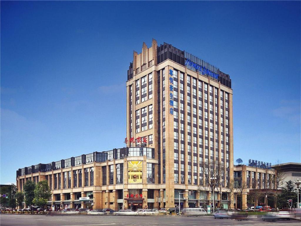 成都Howard Johnson Zunyue Hotel Chengdu的一座高大的建筑,前面有一个钟