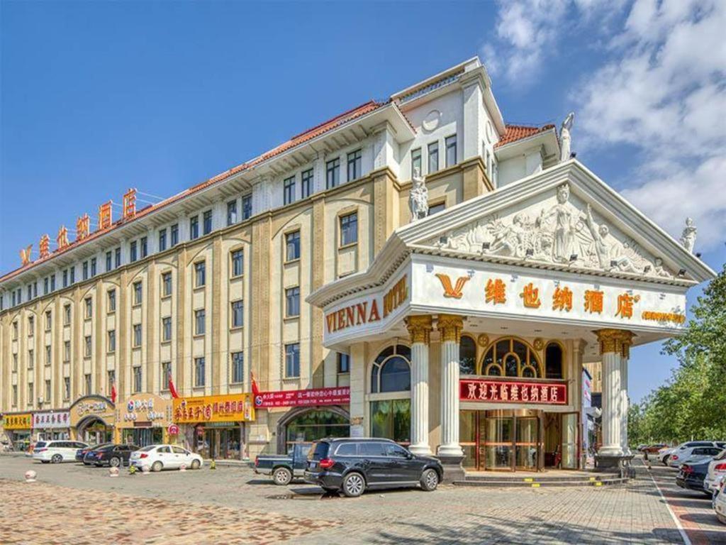 天津Vienna Hotel Tianjin Huaming的一座大型建筑,前面有汽车停放