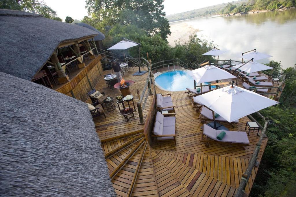 MkalinzuSerena Mivumo River Lodge的户外甲板设有游泳池、桌子和遮阳伞