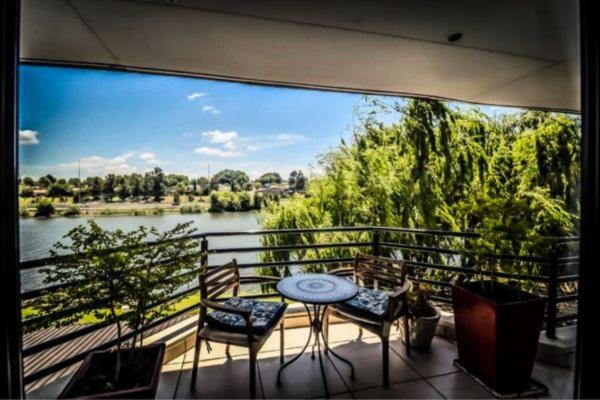 伯诺尼ANEW Hotel & Convention Centre OR Tambo Johannesburg的阳台配有桌椅,享有河景