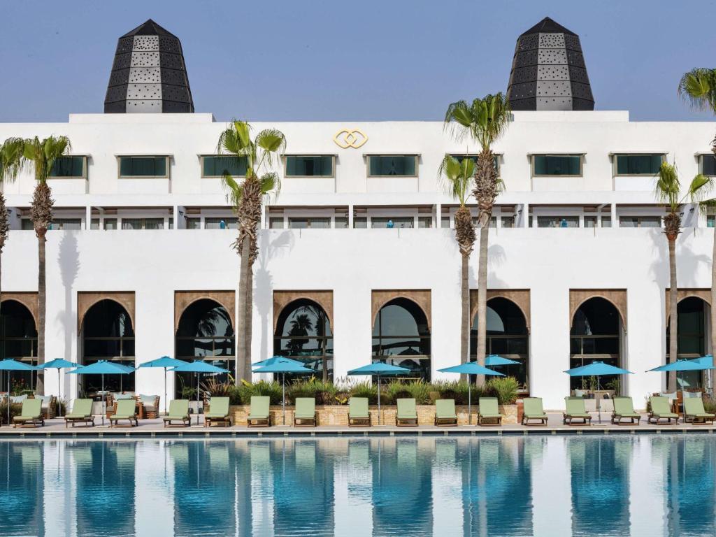 阿加迪尔Sofitel Agadir Royal Bay Resort的一座拥有游泳池、棕榈树和蓝伞的酒店