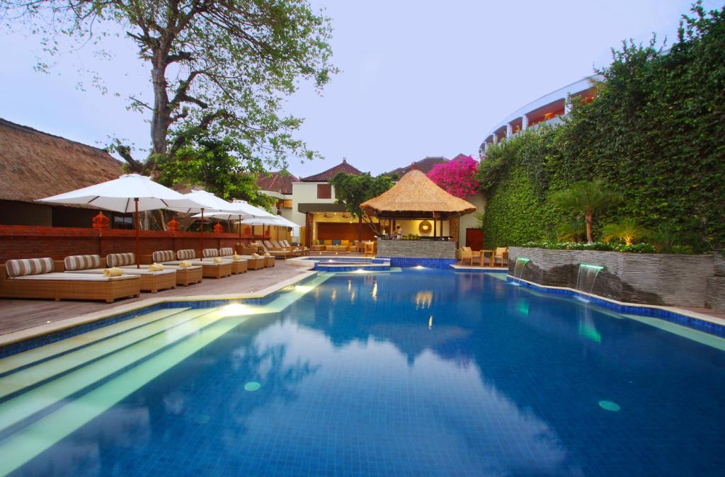 库塔AlamKulkul Boutique Resort的度假村的游泳池配有椅子和遮阳伞