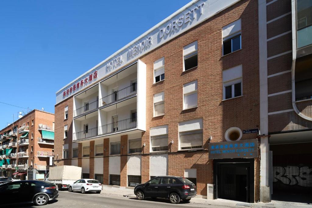 马德里Menoir Dorsett Madrid Usera的一座砖砌建筑,前面有汽车停放