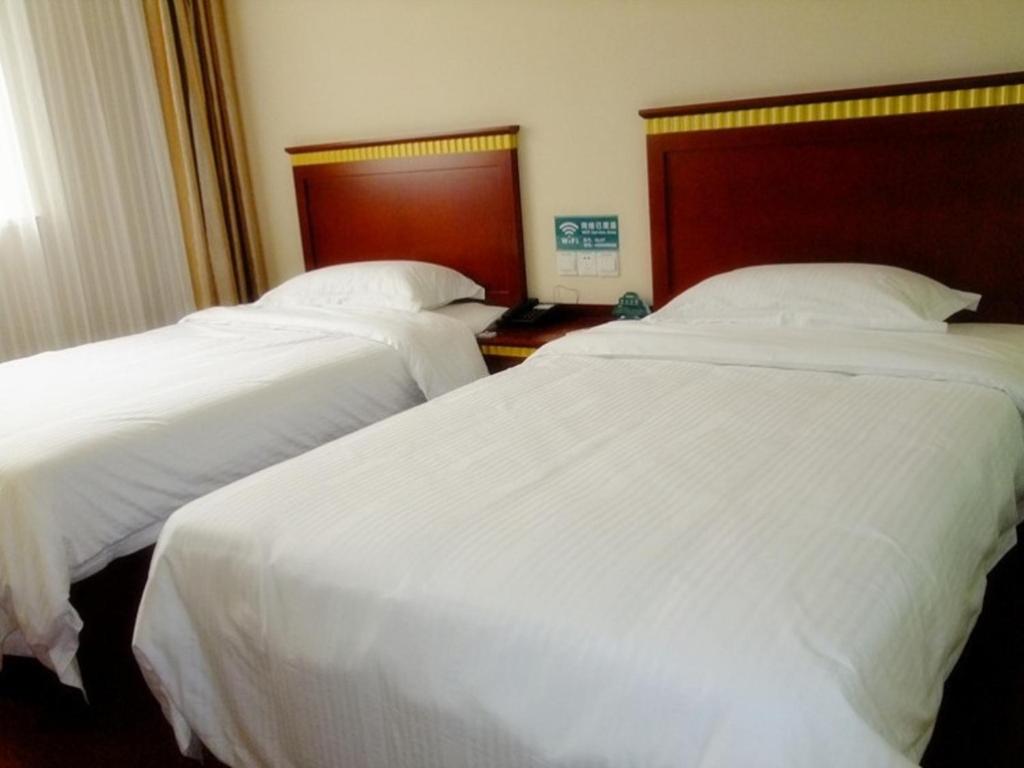 黄山市格林豪泰安徽省黄山市新安江景区天都大道商务酒店的配有白色床单的酒店客房内的两张床