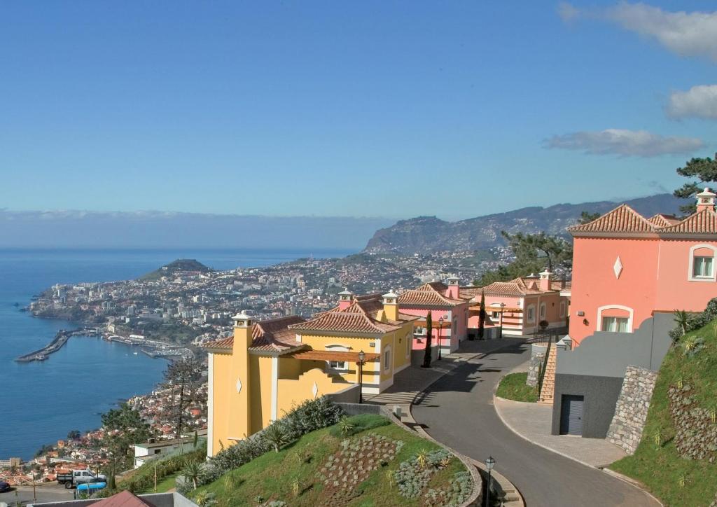 丰沙尔Balancal Apartments and Villas Palheiro Village的山丘上的城镇,以海洋为背景