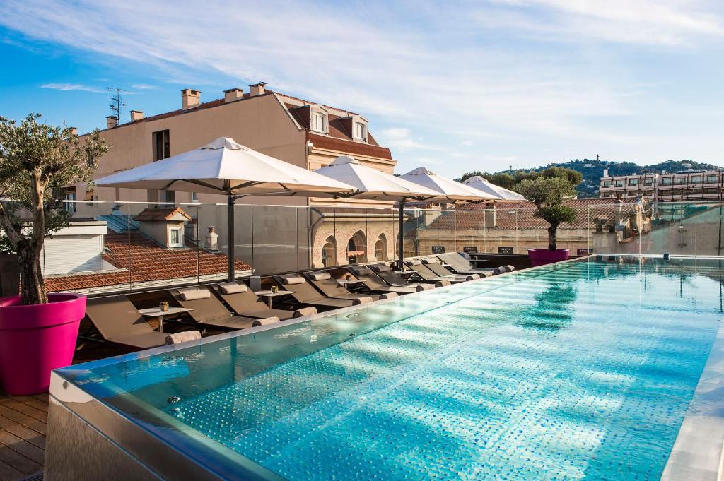 戛纳Five Seas Hotel Cannes, a Member of Design Hotels的一座带椅子和遮阳伞的建筑屋顶游泳池