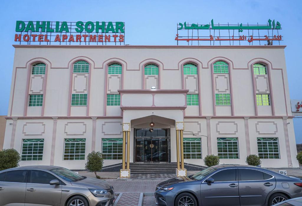 索哈尔Dahlia Sohar Hotel Apartments的两辆汽车停在大楼前