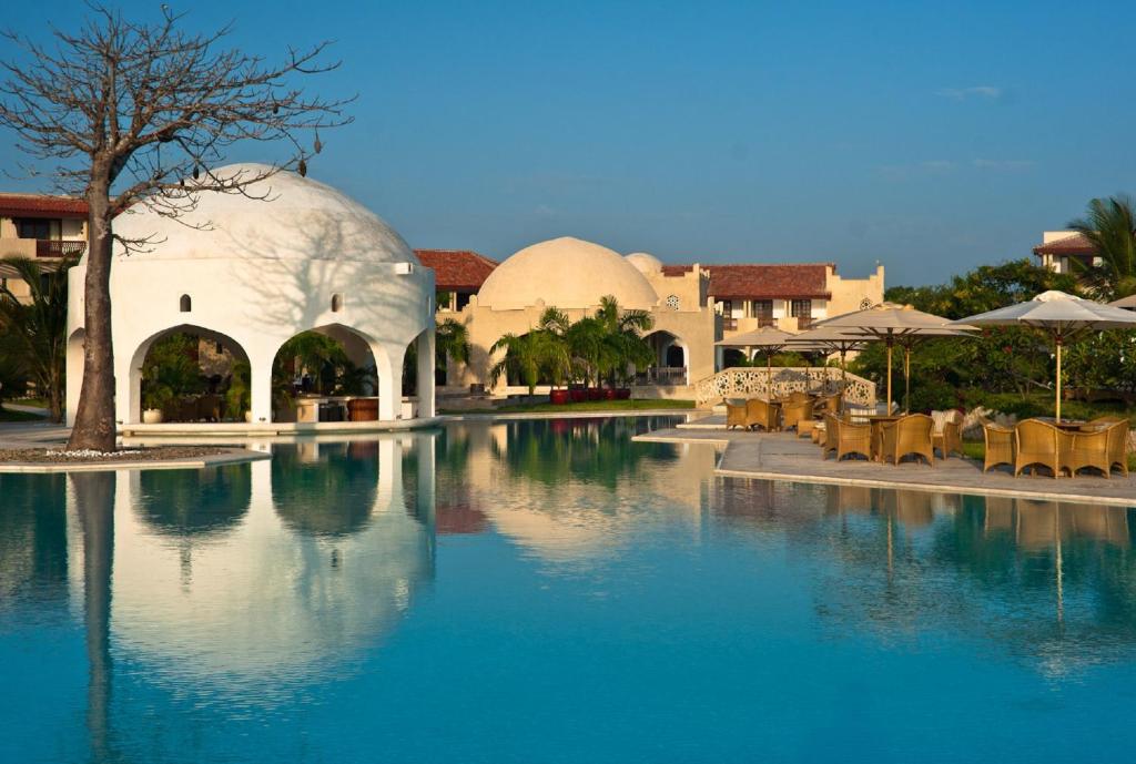 迪亚尼海滩斯瓦希里海滩度假村的度假村内的一个水池,配有桌子和遮阳伞