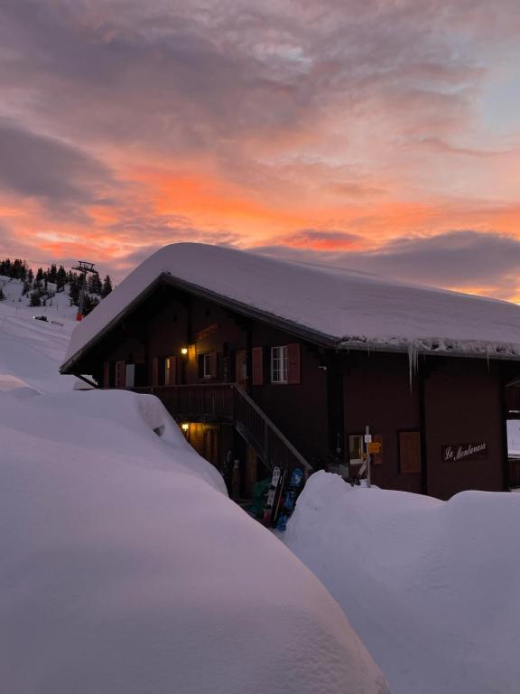 贝特默阿尔卑Chalet La Montanara的一座被雪覆盖的建筑,背景是日落