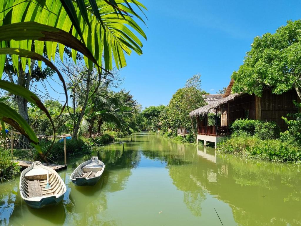 芹苴Green Village Mekong的两艘船停靠在房屋旁边的一条河上