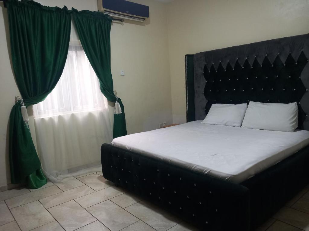贝宁城Tovia Hotel and Suite Limited的一间卧室，配有一张带绿色窗帘的床和一扇窗户