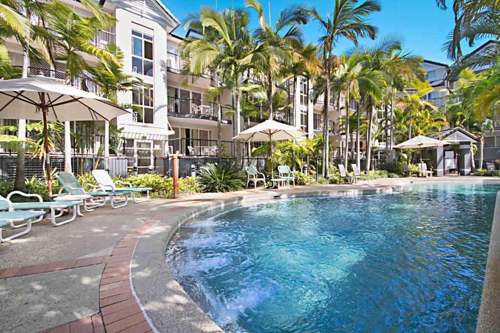 黄金海岸蓝水公寓酒店的一座带椅子和遮阳伞的游泳池位于一座建筑旁边