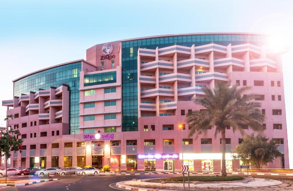 迪拜迪拜兹切公寓式酒店的一座粉红色的建筑,前面有一棵棕榈树