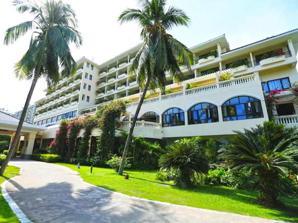 三亚三亚椰林滩大酒店 的一座白色的大建筑,前面有棕榈树