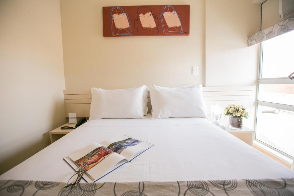 巴西利亚维罗那哈普拉斯长住公寓式酒店的卧室配有一张白色的床,上面有书