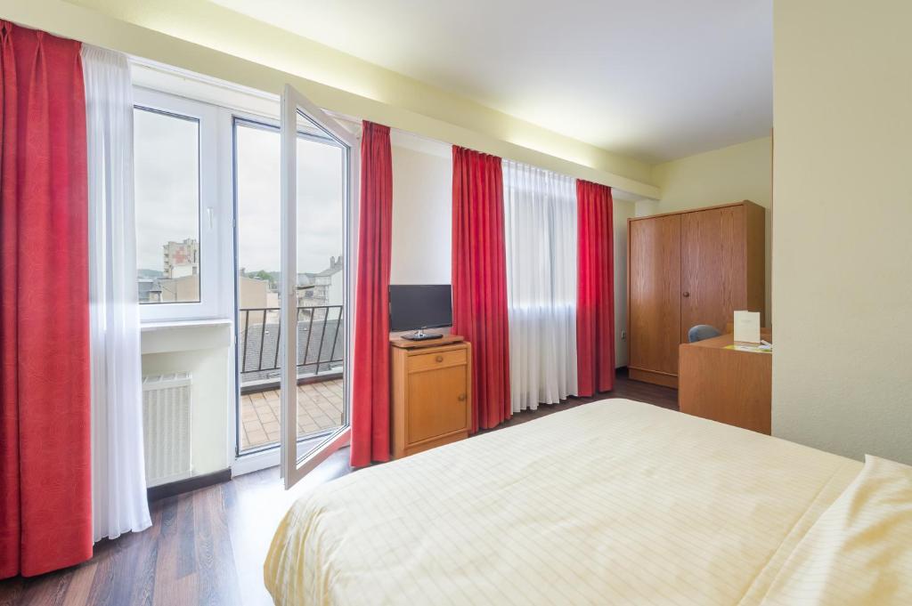 阿尔泽特河畔埃施Logis Hôtel Acacia的一间带红色窗帘和床的卧室以及一个阳台