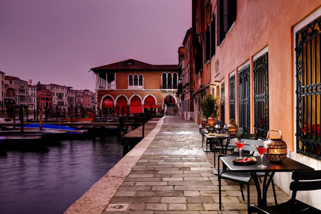 威尼斯Hotel L'Orologio - WTB Hotels的一条运河,旁边是一座建筑,配有桌椅