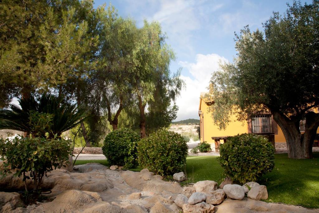 阿尔阿马德穆尔西亚El Mirador de Gebas的一座种有岩石和树木的花园以及一座黄色的房子