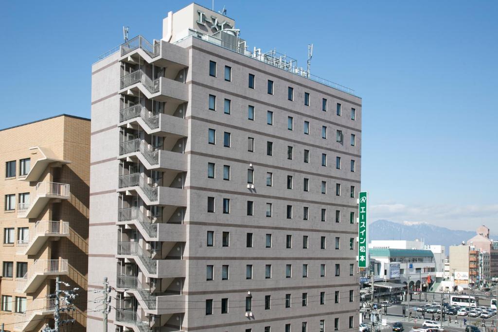 松本松本艾斯旅馆的一座高大的灰色建筑,上面有绿色的标志