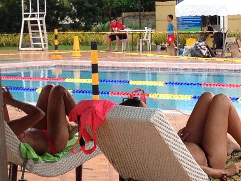 马尼拉爱丽舍城堡公寓式酒店的两人躺在游泳池旁的椅子上