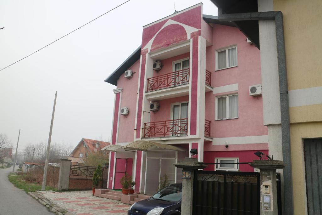 贝尔格莱德Kuca Veljovica的一座粉红色的建筑,前面有一辆汽车