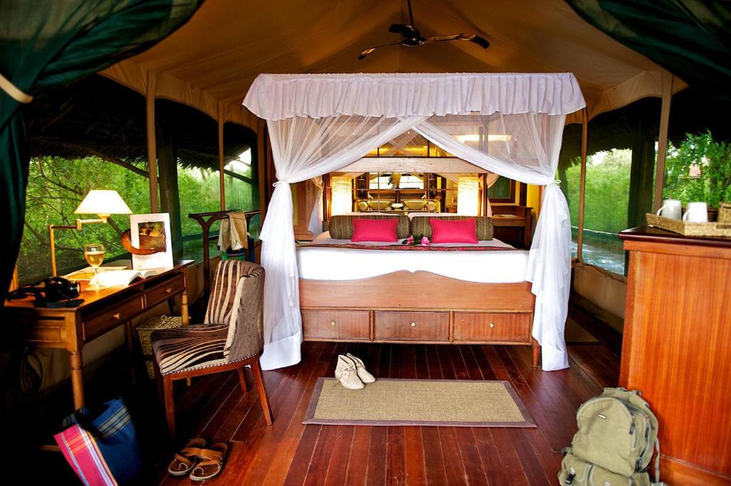 Archers PostSamburu Intrepids Tented Camp的一间卧室配有一张床、一张桌子和一张四柱床。