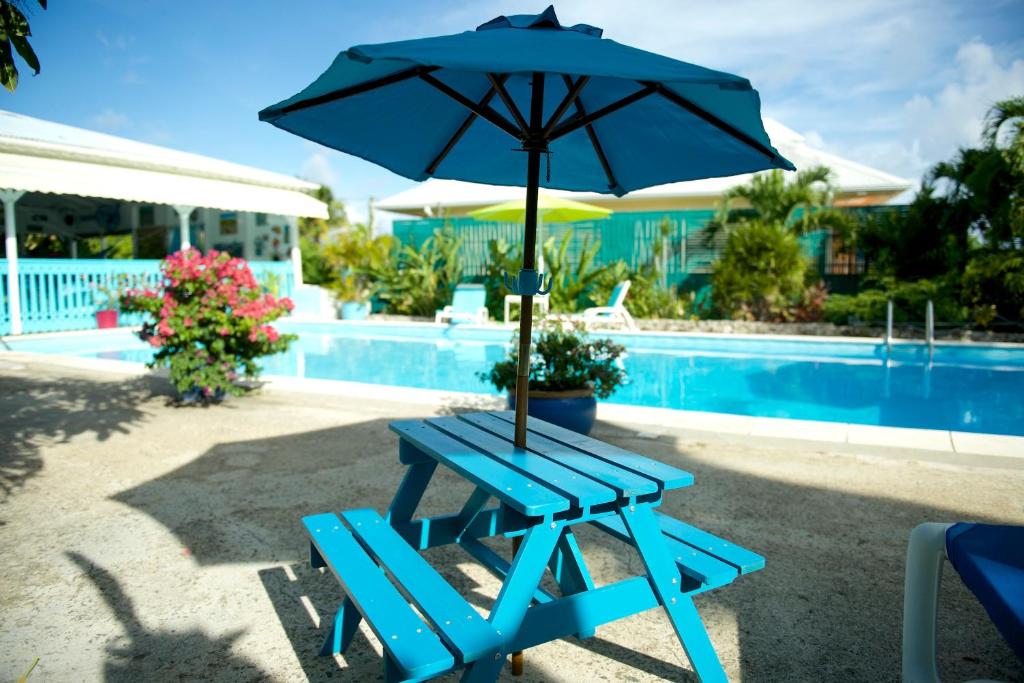哥西尔Hotel Cap Sud Caraibes的蓝色野餐桌,泳池旁配有遮阳伞