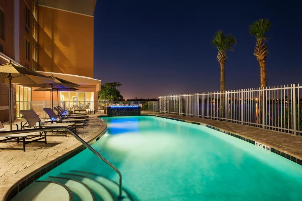迈阿密迈阿密机场坎布里亚酒店 - 蓝色泻湖的游泳池,晚上配有椅子和棕榈树