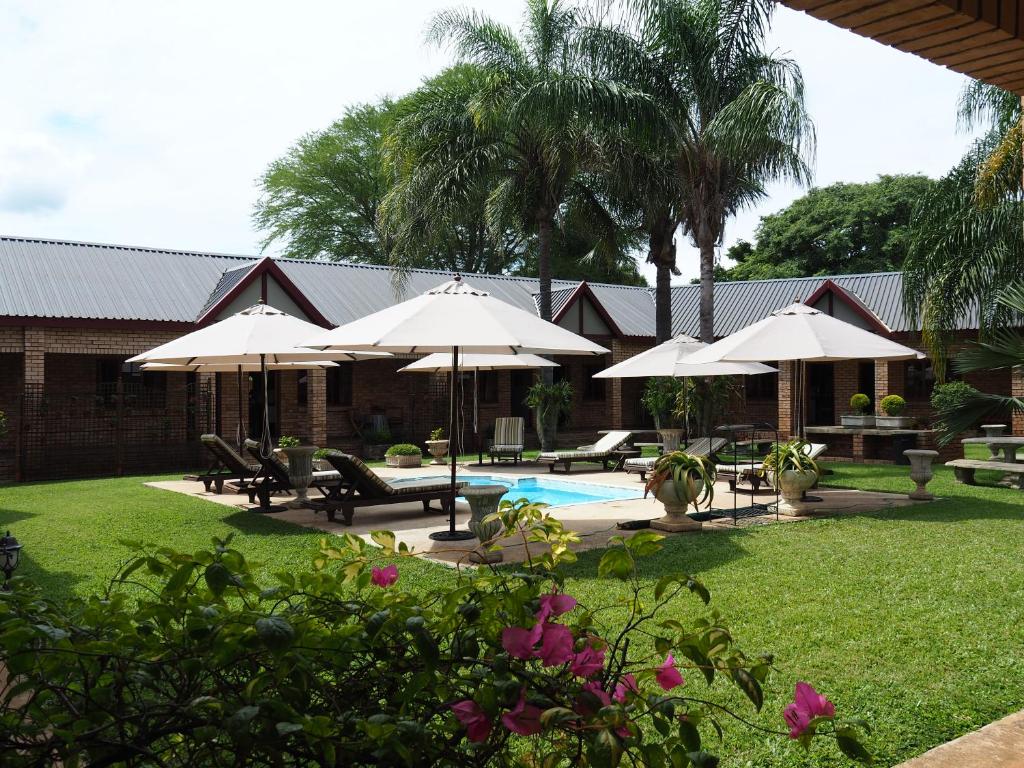 蓬戈拉Kwalala Lodge的一个带遮阳伞的庭院和一个带桌椅的游泳池。