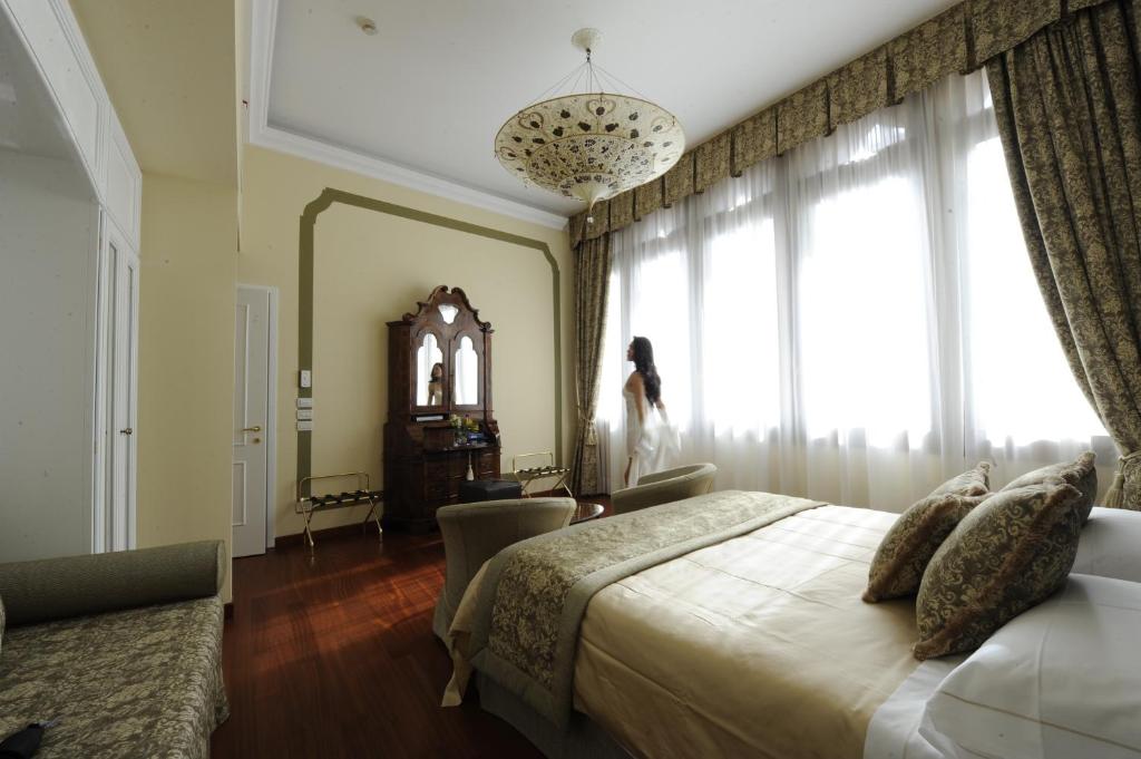 威尼斯乐索雷酒店的卧室配有床,女士站在窗户旁