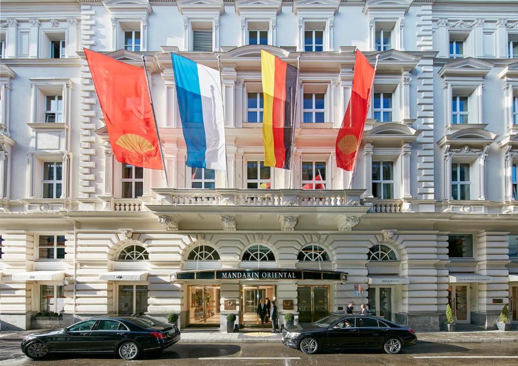慕尼黑Mandarin Oriental, Munich - Germany's Best City Hotel 2024的两辆汽车停在一座悬挂着旗帜的建筑前