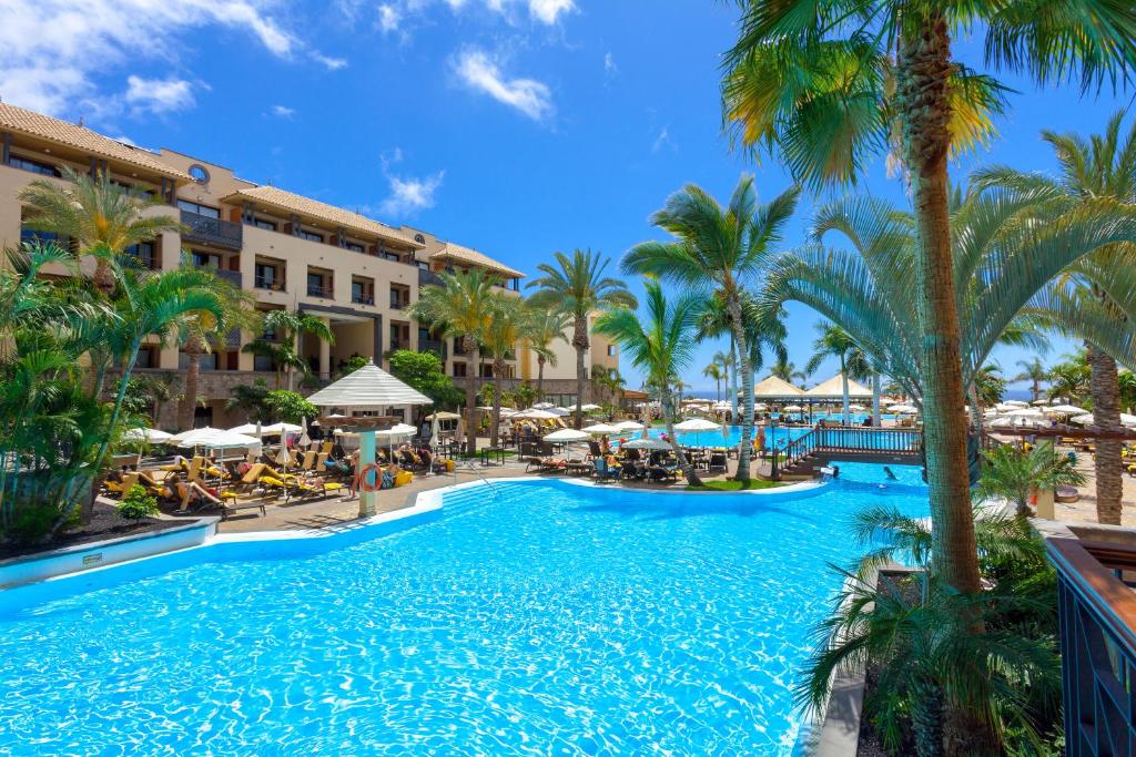 阿德耶阿德赫格瑞考斯塔酒店的度假村的游泳池拥有棕榈树和遮阳伞