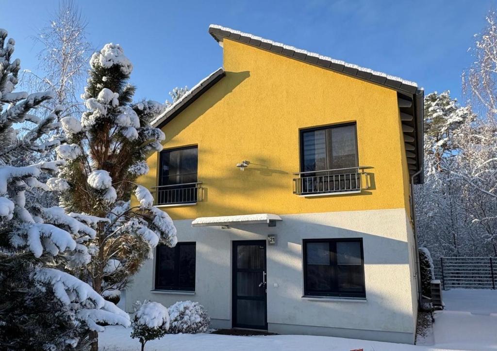 柏林Ferienpark Rübezahl am Müggelsee, Haus 21 Efeu mit eigener Sauna, idealer Ort für Natur- und Erholungssuchende, für Radfahrer, Familien mit Kindern und Hundeliebhaber的雪中的一个黄色和白色的房子
