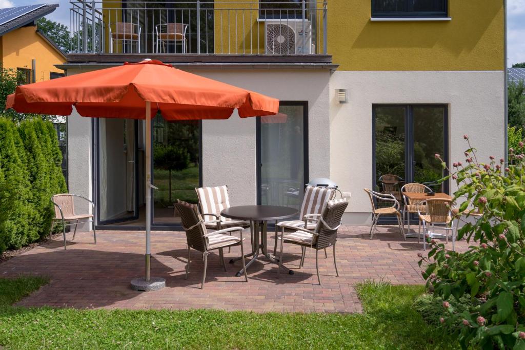 柏林Ferienpark Rübezahl am Müggelsee, Haus 18 Schlehe mit eigener Sauna, idealer Ort für Natur- und Erholungssuchende, für Radfahrer und Familien mit Kindern的露台上的一张桌子、几把椅子和一把遮阳伞