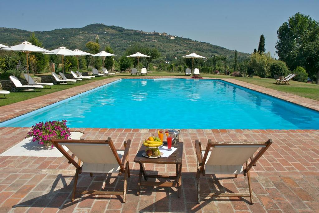 科尔托纳笆尔德立别墅酒店的游泳池旁设有两把椅子和一张桌子